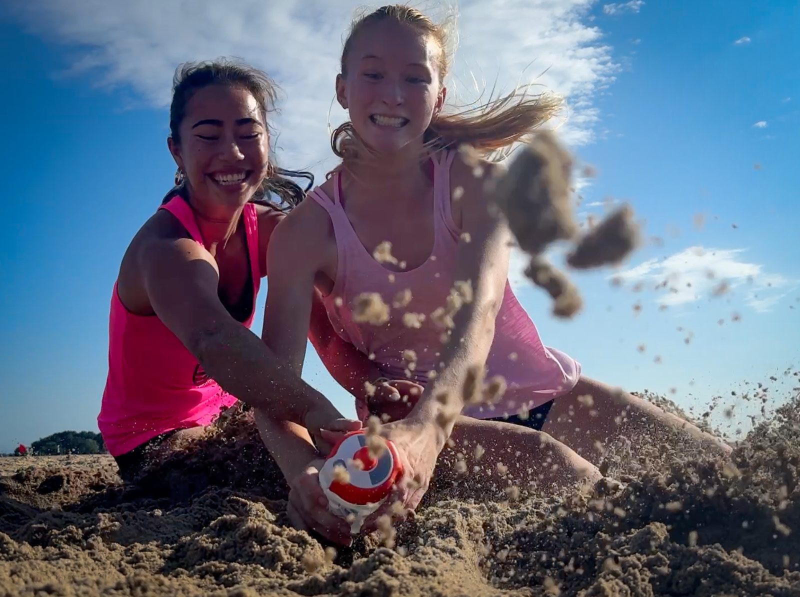 Two athletes mid-dig at the beach, sand flying