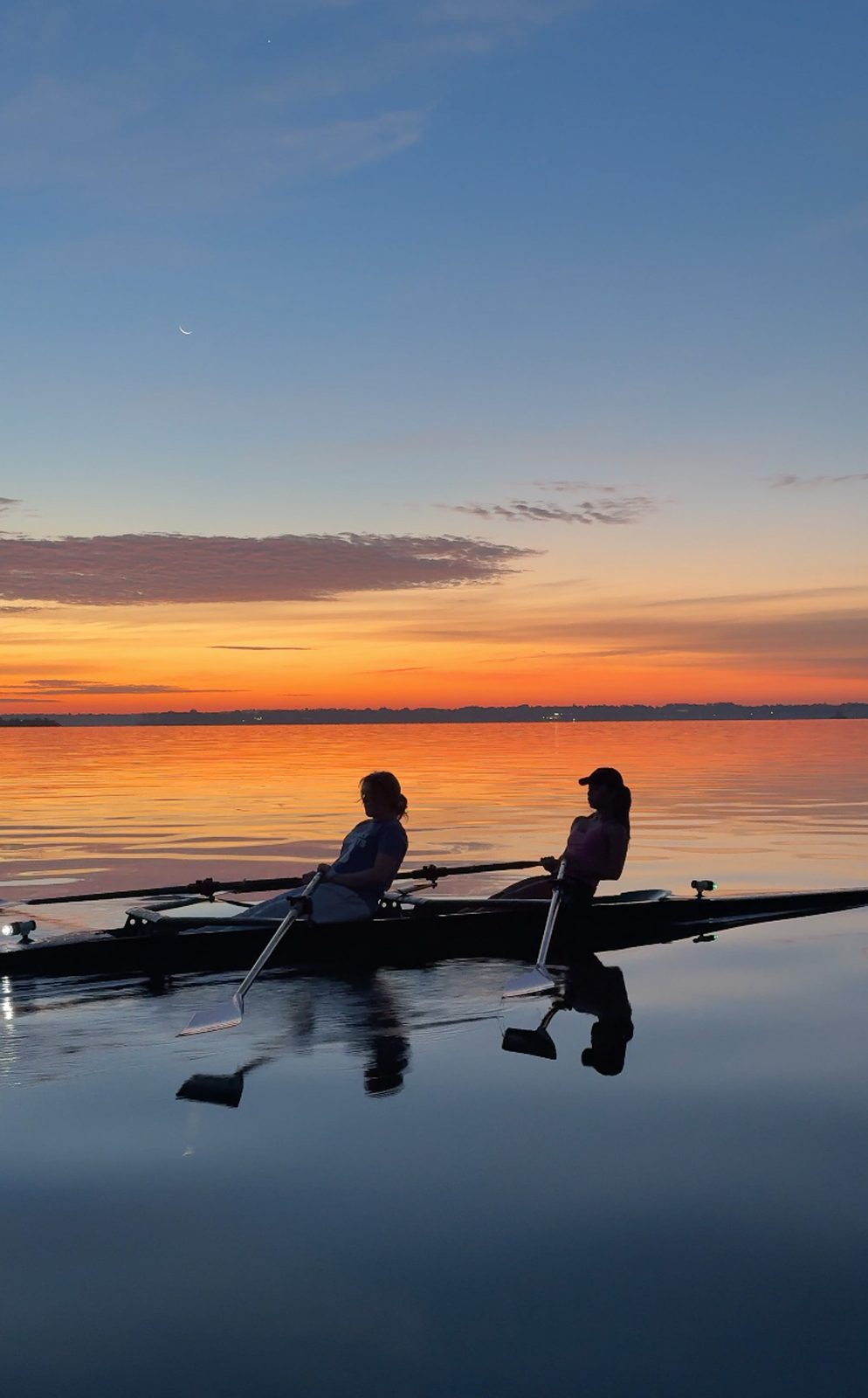 Two rowers in a double at first light, the sky turning gold