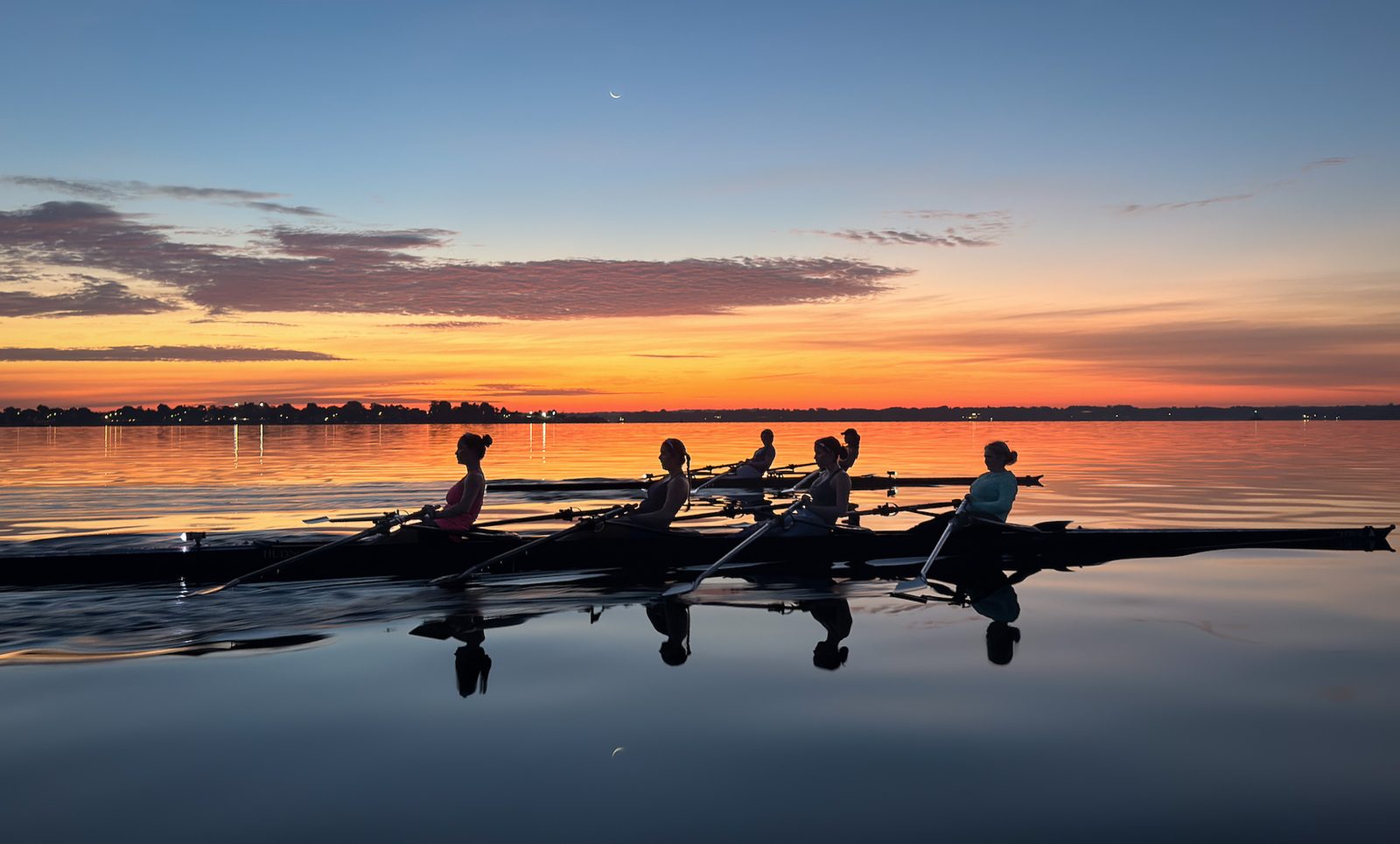 A quad silhouetted against the orange dawn, oars resting on still water