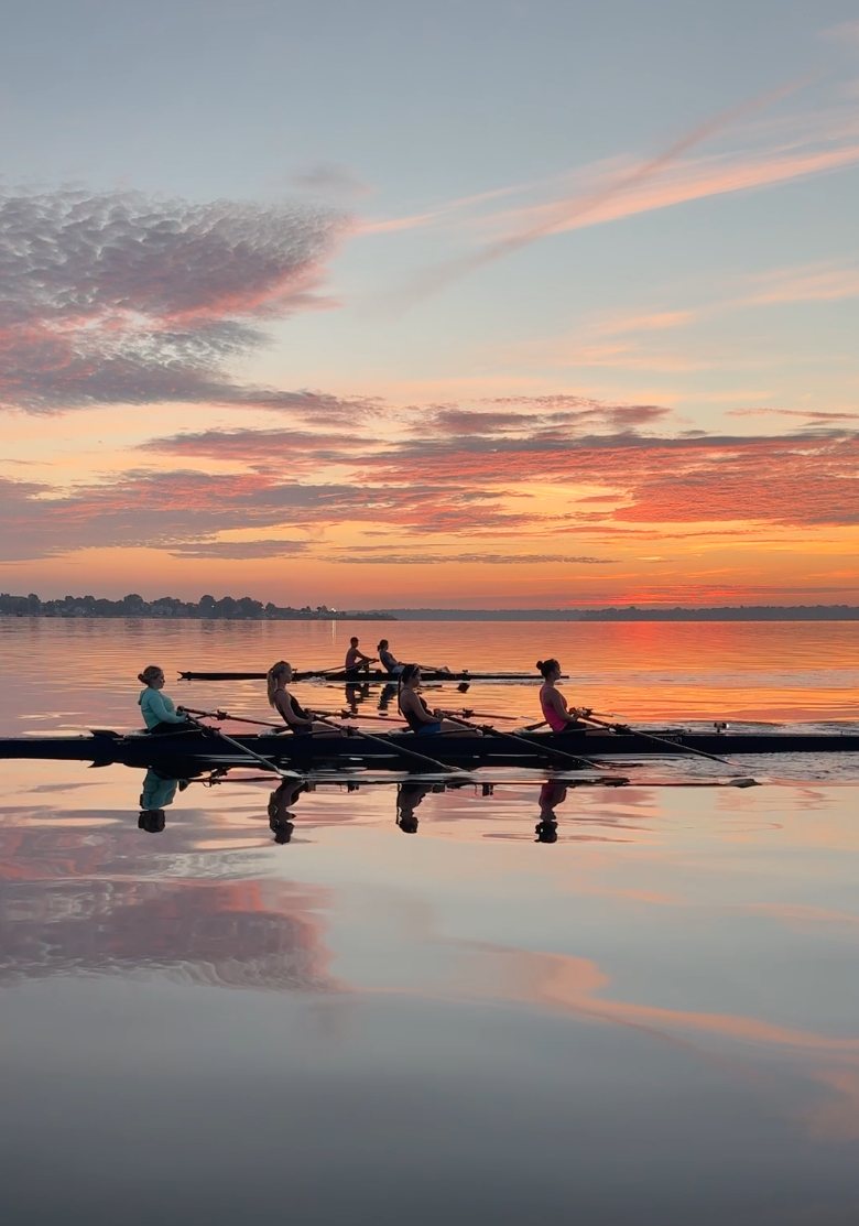 A quad and a double on glass-calm water under a spectacular orange sunrise