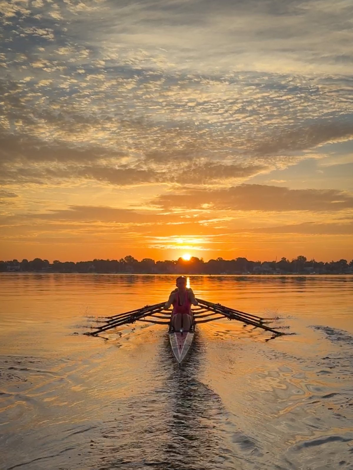 A single sculler rowing straight into the sunrise