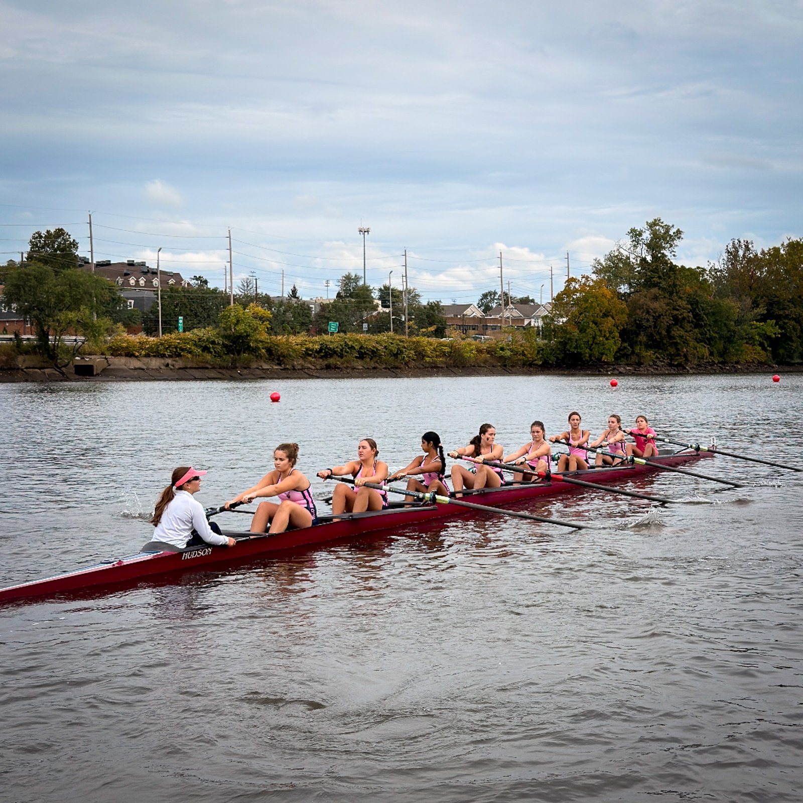 An eight in pink rowing between green riverbanks
